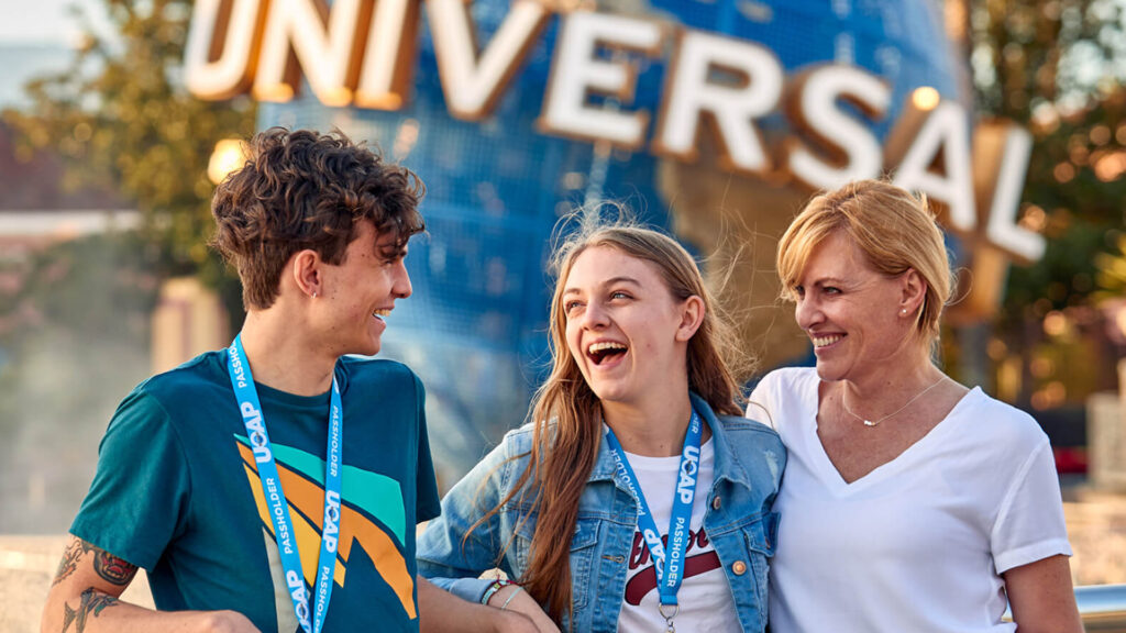 Three smiling theme park guests wearing passholder lanyards celebrating in front of the Universal globe.