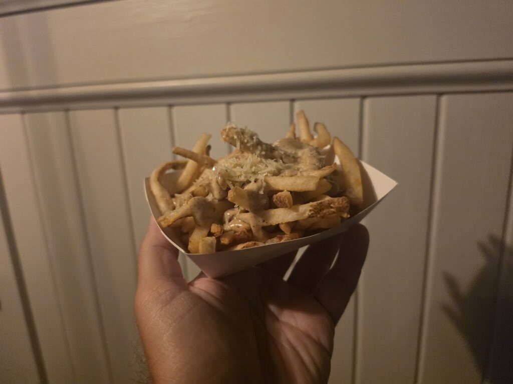Hand holding a paper food boat filled with Black Garlic, Truffle, and Parmesan Fries served at Columbia Harbour House in Magic Kingdom.