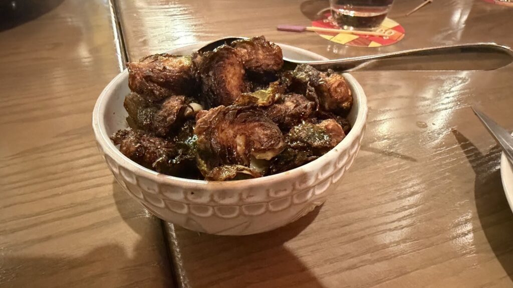 Crispy, roasted Brussels sprouts served in a textured white ceramic bowl on a wooden table.