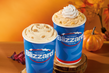 Two Dairy Queen Blizzard cups on wooden coasters, one topped with whipped cream, set against an autumn background with fall leaves and a pumpkin.