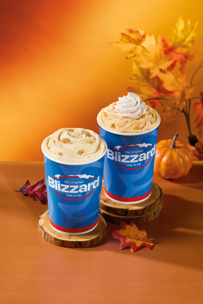 Two Dairy Queen Blizzard cups on wooden coasters, one topped with whipped cream, set against an autumn background with fall leaves and a pumpkin.