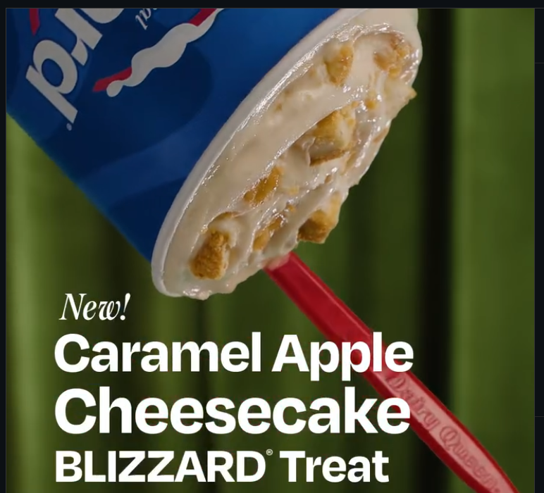 A Dairy Queen Blizzard cup held upside down with a red spoon, featuring a Caramel Apple Blizzard Cheesecake flavor with visible chunks against a green background.