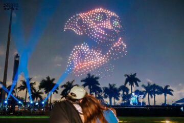 A couple sitting on a lawn watching a night drone show illuminating a large image of Dobby the house-elf from Harry Potter in the sky during Harry Potter Drone Show