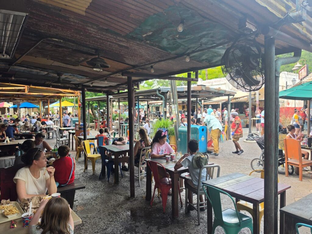 The covered outdoor dining area at Harambe Market in Disney's Animal Kingdom, filled with guests sitting at tables under a rustic roof.