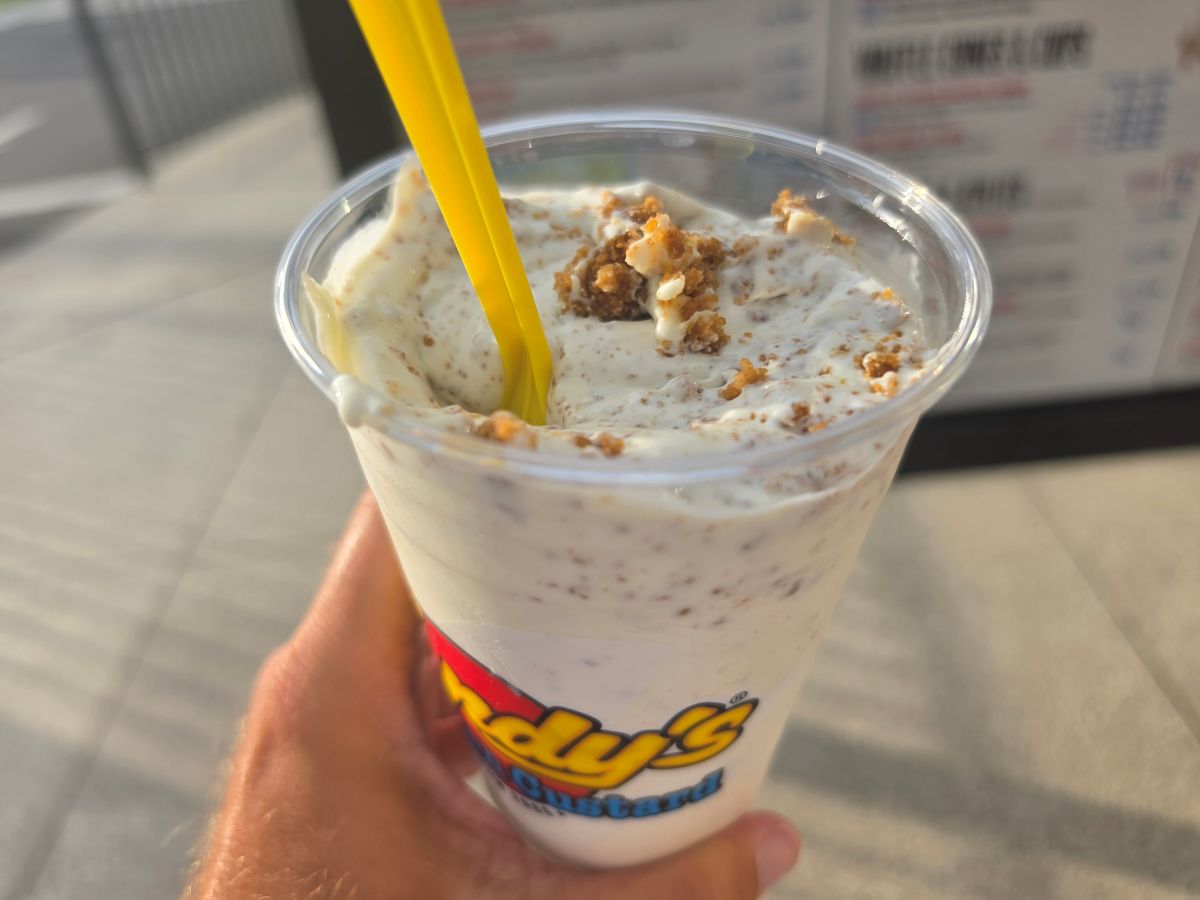 Close-up of a hand holding a Key Lime Pie Concrete from Andy's Frozen Custard, showing thick frozen custard blended with graham cracker crust pieces.