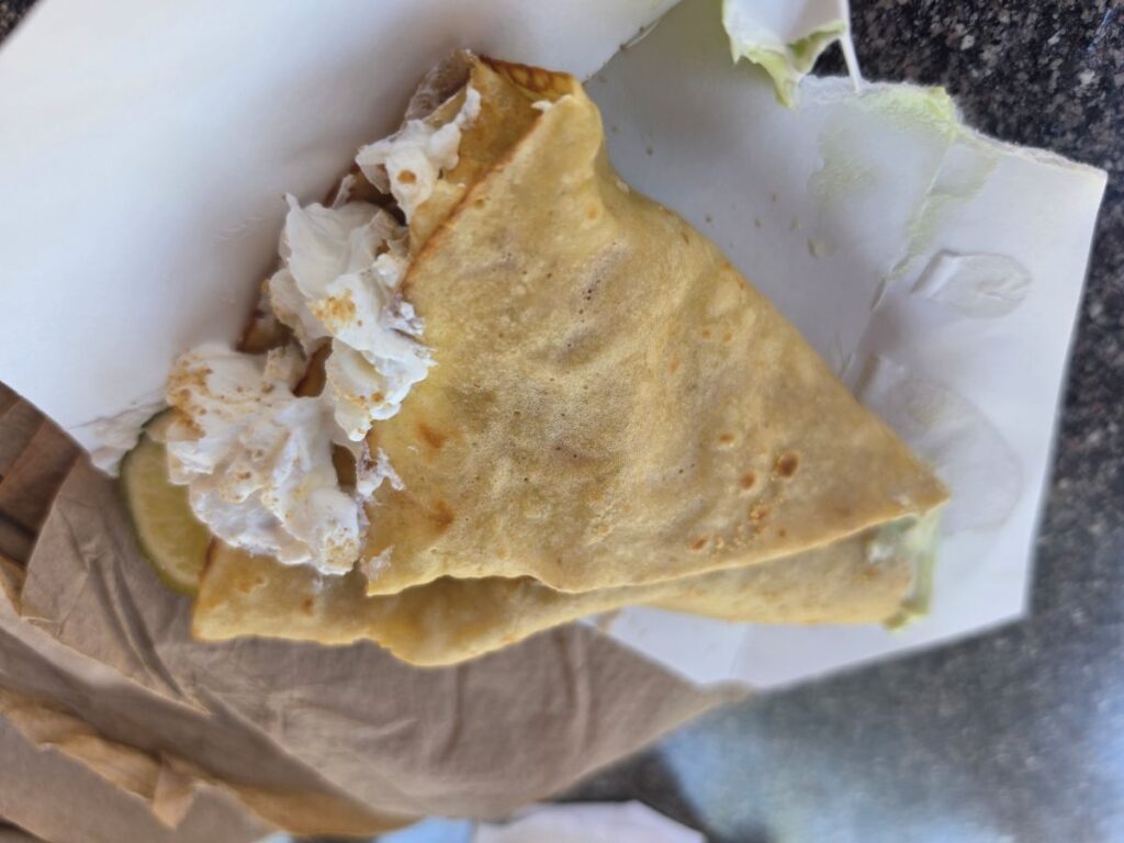 A close-up side view of a folded crepe resting on white wrapper paper, showcasing the creamy filling inside and a lime slice on the side.