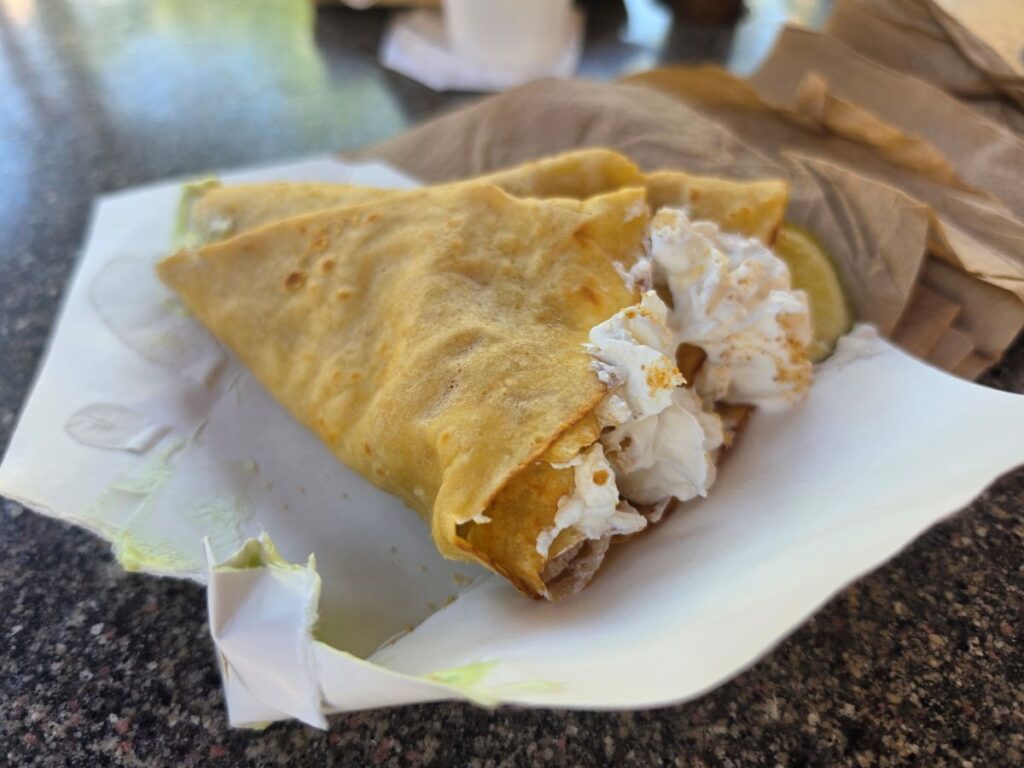 A close-up side view of a folded crepe resting on white wrapper paper, showcasing the creamy filling inside and a lime slice on the side.