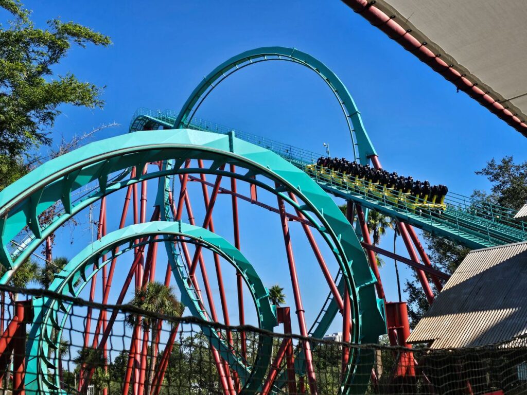 A full yellow coaster train climbing the massive lifthill of Kumba under a bright blue sky at Busch Gardens.
