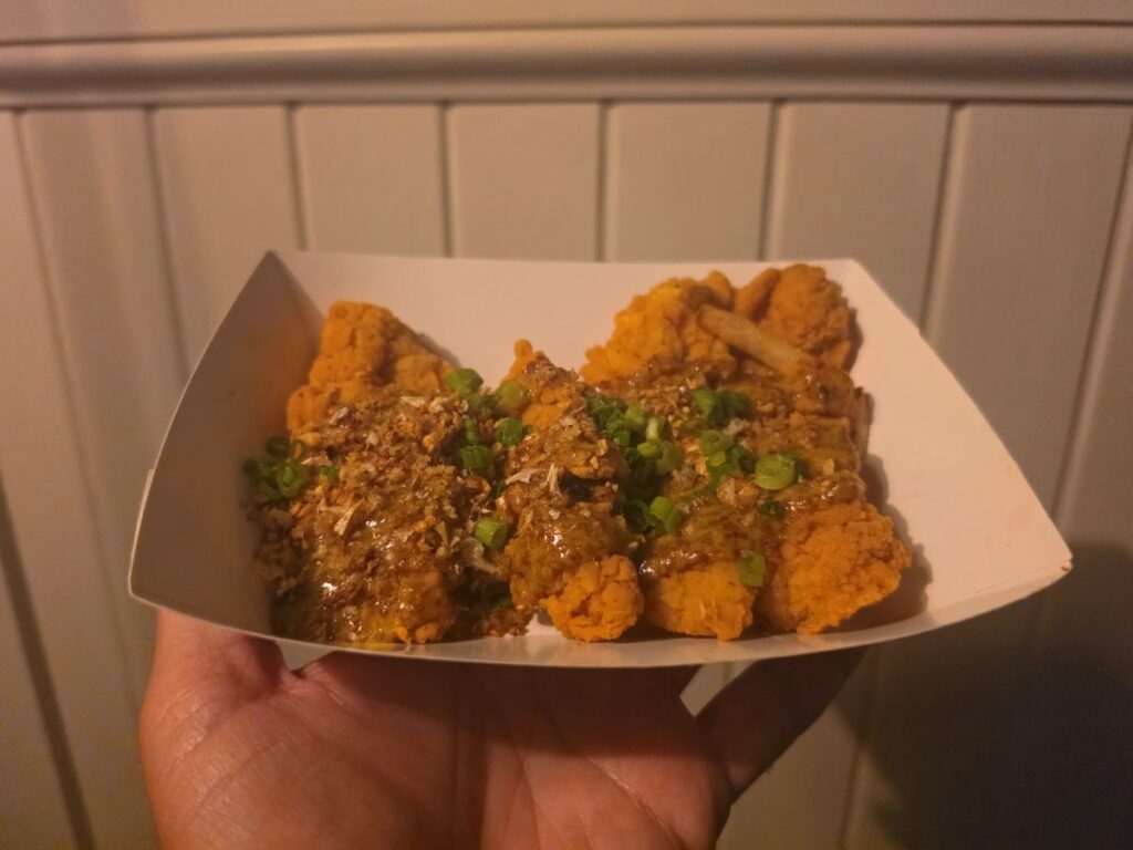 Front-facing view of a paper tray filled with Maple-Mustard Chicken Strips garnished with savory sauce and fresh green onions from Columbia Harbour House.