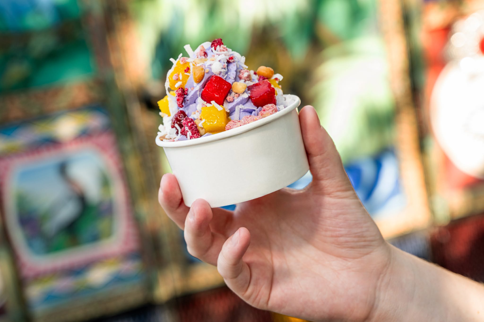 One of the Moana Disney Treats -pineapple soft-serve float in a clear cup topped with colorful candy pieces, a green and white striped straw, and a fresh pineapple wedge coated in toasted coconut.