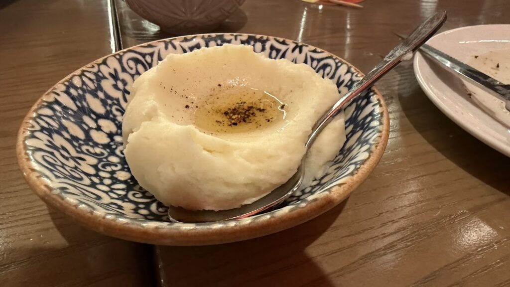 Smooth olive oil potato puree served in a blue and white patterned bowl with a pool of olive oil and cracked black pepper in the center.