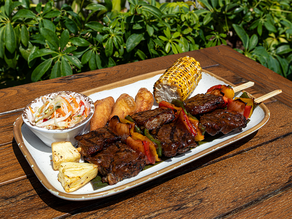 Tender grilled steak skewers served with peppers, pineapple wedges, grilled corn, festival bread, and slaw at Bob Marley – A Tribute to Freedom.
