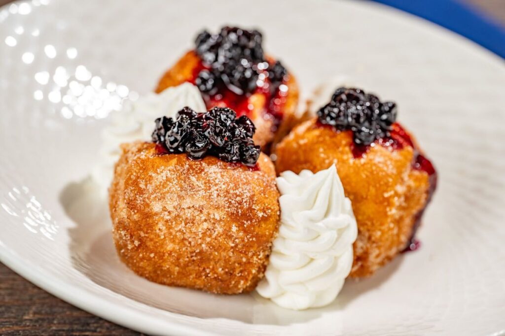Cinnamon-sugar dusted stuffed French toast bite-sized cubes topped with berry compote and whipped cream at Ale & Compass breakfast.