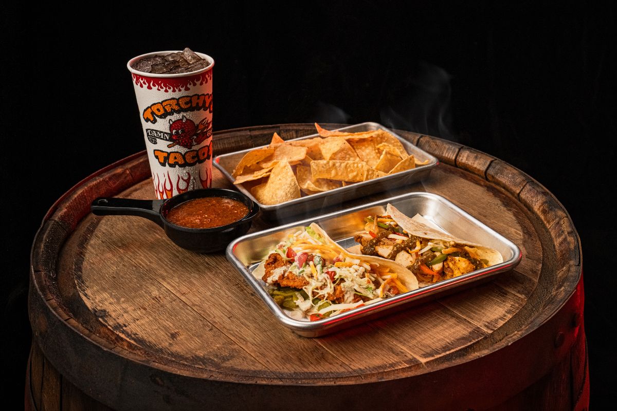 A wooden barrel featuring two food containers and a beverage, creating a charming outdoor dining atmosphere that promotes the Torchy's Taco deal.
