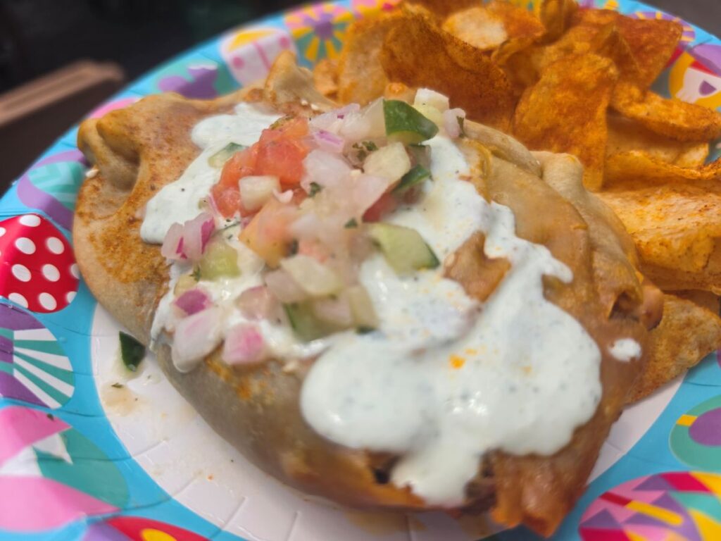 Extreme close-up of a savory Tanzanian Meat Pie showing the golden-brown crust topped with tzatziki-style sauce and diced vegetable salsa.