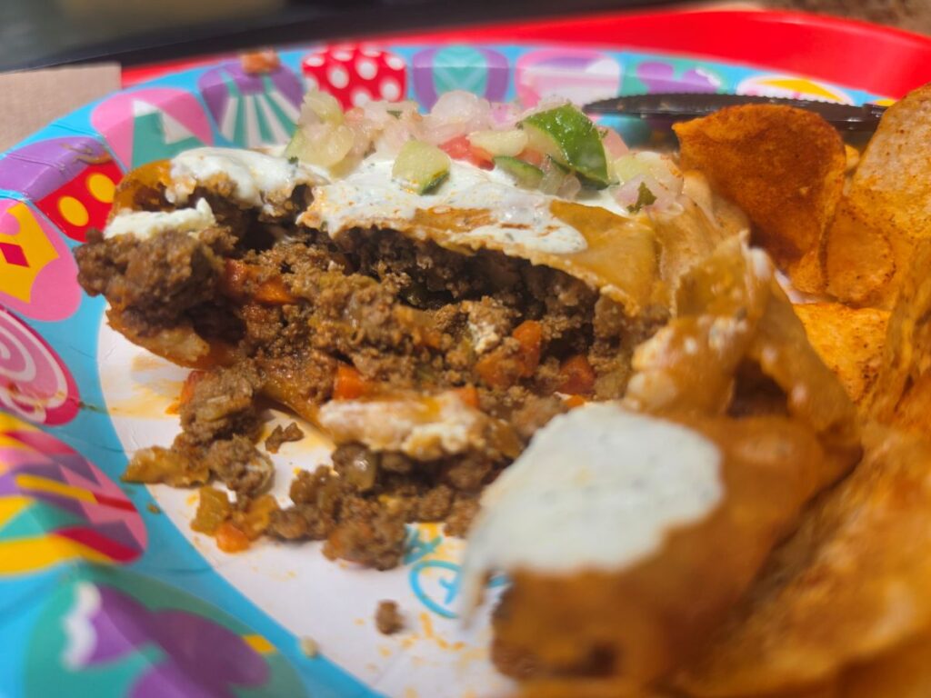 A Tanzanian Meat Pie cut open on a plate, revealing a rich, savory ground meat and vegetable filling inside the baked pastry crust.
