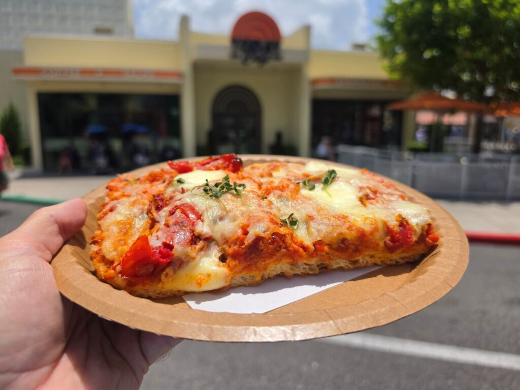 A close-up view of a freshly baked Tomato Mozzarella Flatbread on a paper plate being held outside TODAY Cafe.