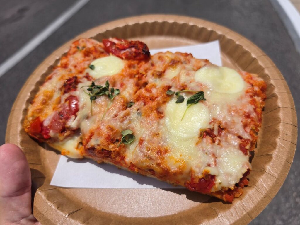 Top-down close-up view of a thick-crust Tomato Mozzarella Flatbread on a paper plate showing melted mozzarella and fresh green herbs.