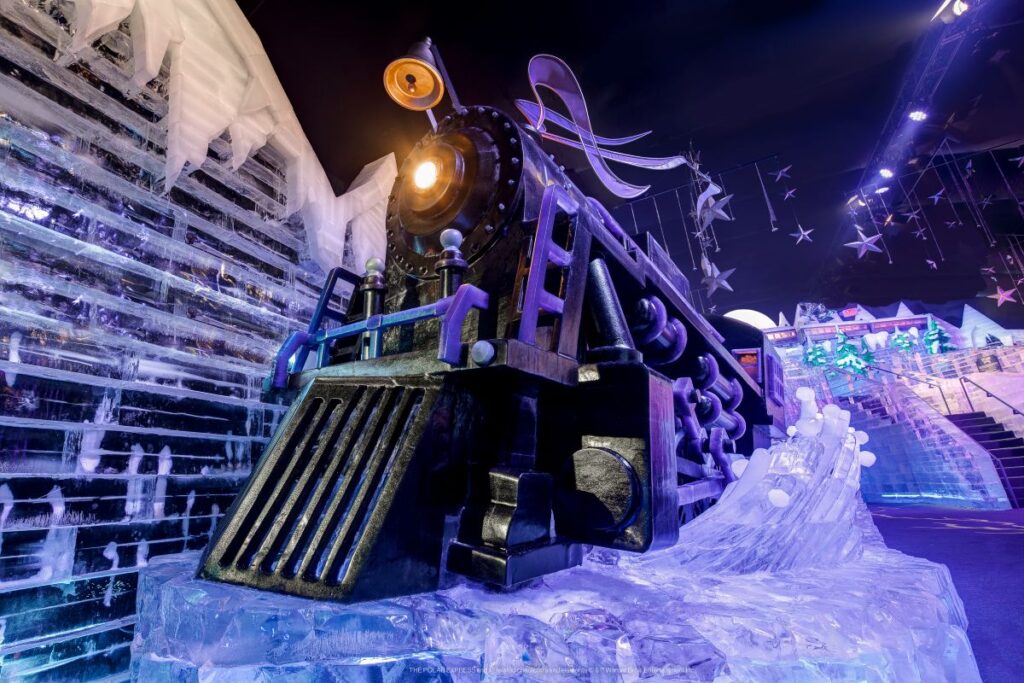 A life-sized steam locomotive ice sculpture illuminated in dramatic purple and blue light inside the ICE Christmas attraction.