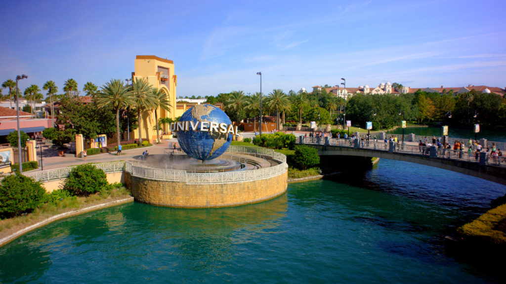 The iconic Universal Studios rotating globe sits at the entrance of Universal Orlando Resort, next to a stone bridge over a clear blue waterway under a sunny sky, serving as a promotion for the Universal Florida Resident Ticket Deal.