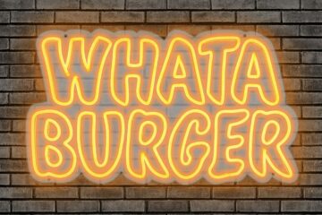 Illuminated yellow and orange Whataburger neon sign mounted on a dark brick wall