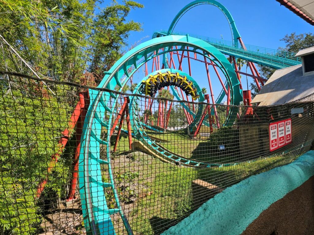 A yellow and black coaster train maneuvers through the teal steel track of Kumba's signature corkscrew elements at Busch Gardens Tampa Bay.