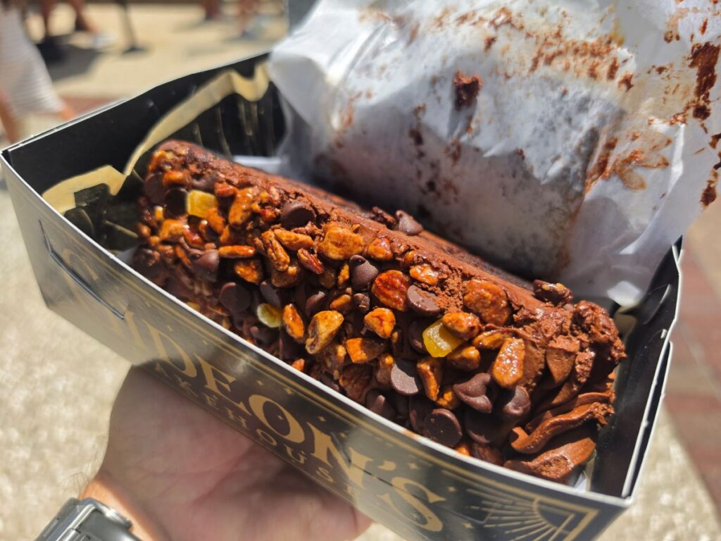 A close-up view of a rich orange pecan chocolate cake slice sitting inside its black and gold bakery box from Gideon's Bakehouse.