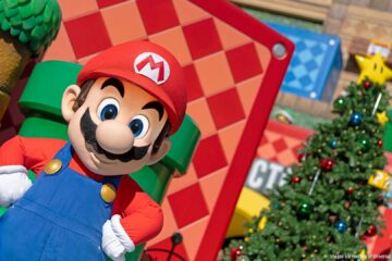 Mario character posing next to a decorated Christmas tree in Super Nintendo World