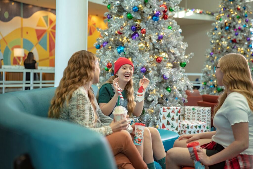 Guests sitting on a sofa near silver Christmas trees inside the lobby of Universal Cabana Bay Beach Resort