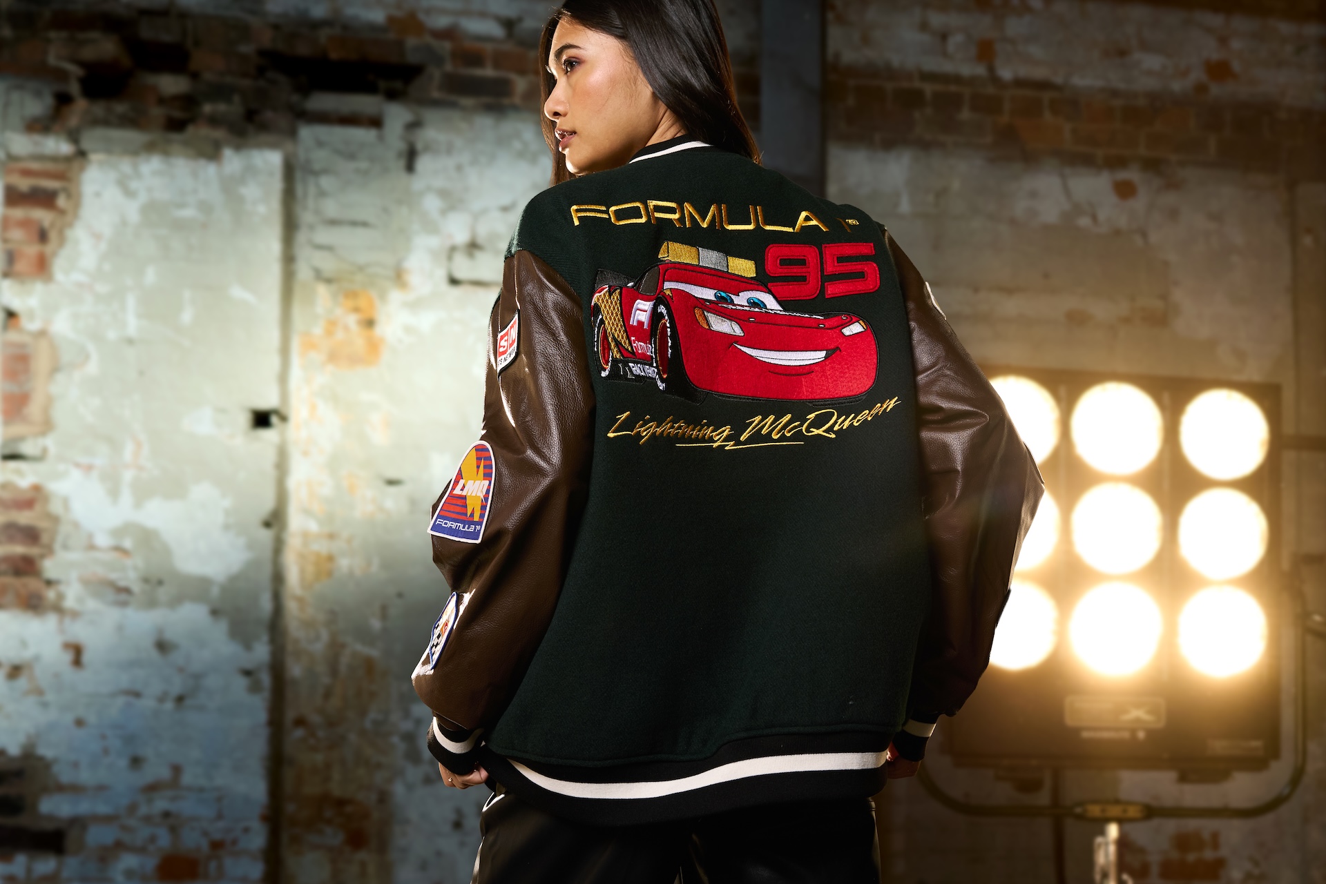 Woman wearing a green and brown Disney Formula 1 varsity jacket featuring Lightning McQueen number 95 embroidered on the back.