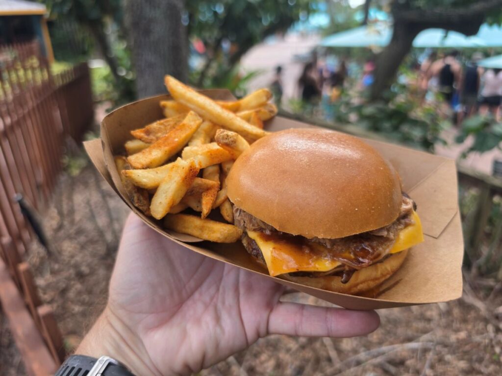 Hand holding a paper tray with a Kookaburra Kitchen BBQ burger topped with pulled pork and a side of seasoned french fries