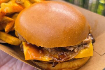 Close-up of a BBQ pulled pork cheeseburger on a soft bun served in a paper boat with fries