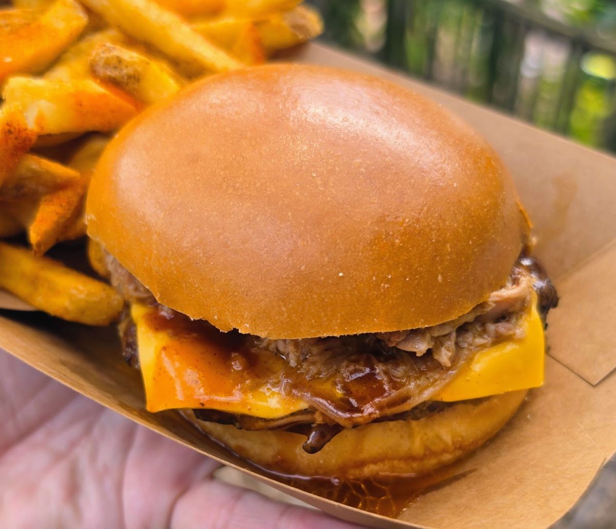 Close-up of a BBQ pulled pork cheeseburger on a soft bun served in a paper boat with fries