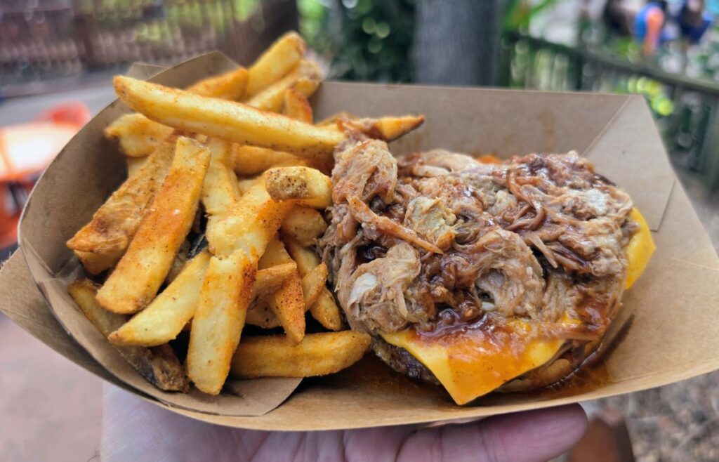 Open-faced view of a BBQ burger piled with pulled pork and melted cheese next to a side of french fries
