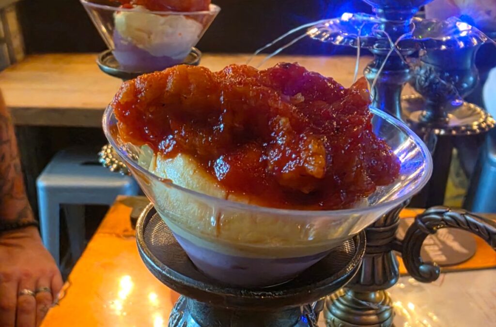Close-up of deviled eggs topped with crispy fried chicken and sweet-and-tart pepper sauce served in a martini glass on a candelabra stand.
