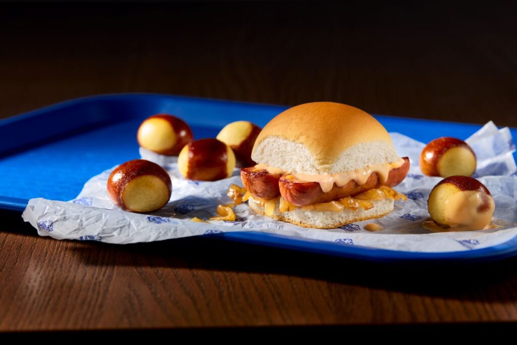 White Castle beer cheese slider served on a wooden board with pretzel bites and a cup of Garage Beer cheese dipping sauce.