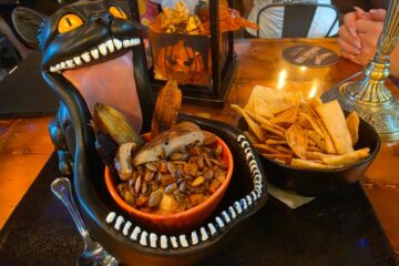 Roasted mixed mushroom and hummus Dark Forest Dip served inside a gaping black cat bowl alongside pita chips and roasted vegetables.