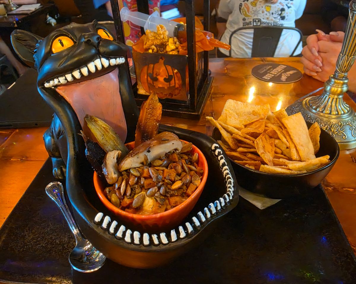 Roasted mixed mushroom and hummus Dark Forest Dip served inside a gaping black cat bowl alongside pita chips and roasted vegetables.