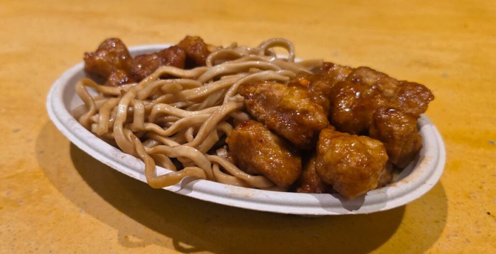 Side-angle view of glazed orange chicken paired with lo mein noodles at Dragon Fire Grill in Busch Gardens Tampa Bay
