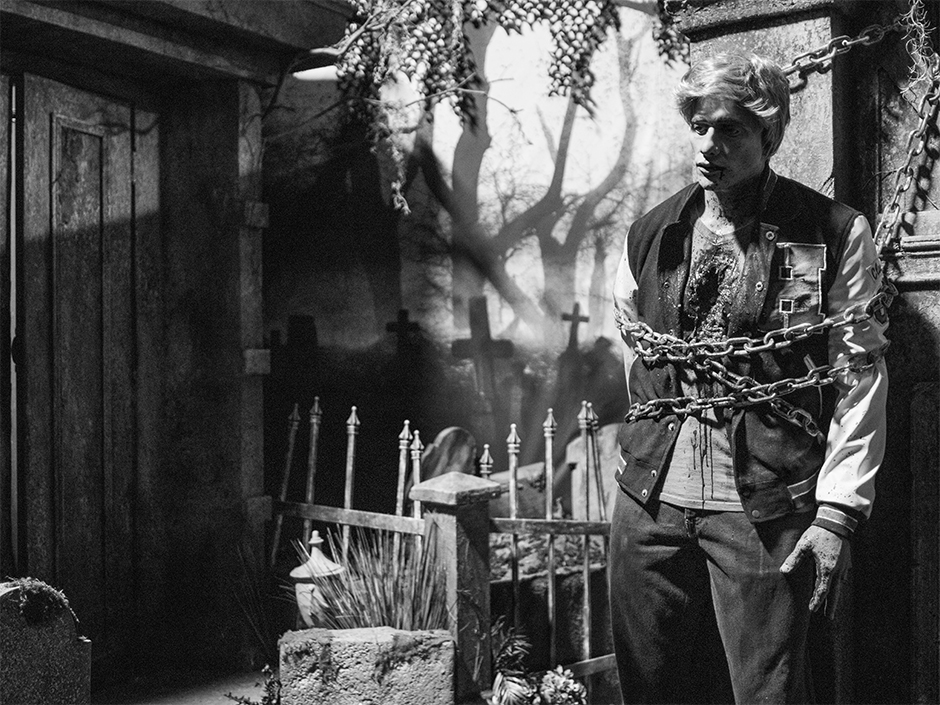 Black and white graveyard scene with a high school jock tied in chains to a tombstone in HHN Bloodengutz 2026 house