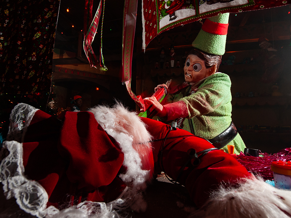 Killer Christmas elf holding a chainsaw attacking Santa Claus on the floor in HHN house