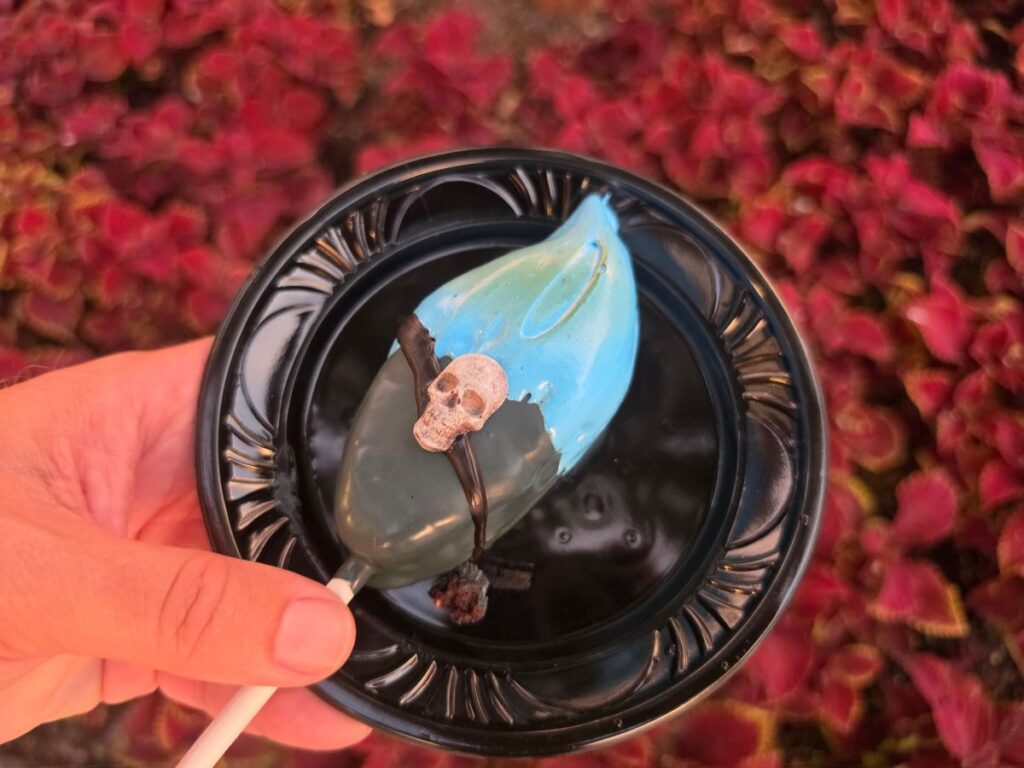 Hand holding a Hades Cake Pop on a stick over red foliage.