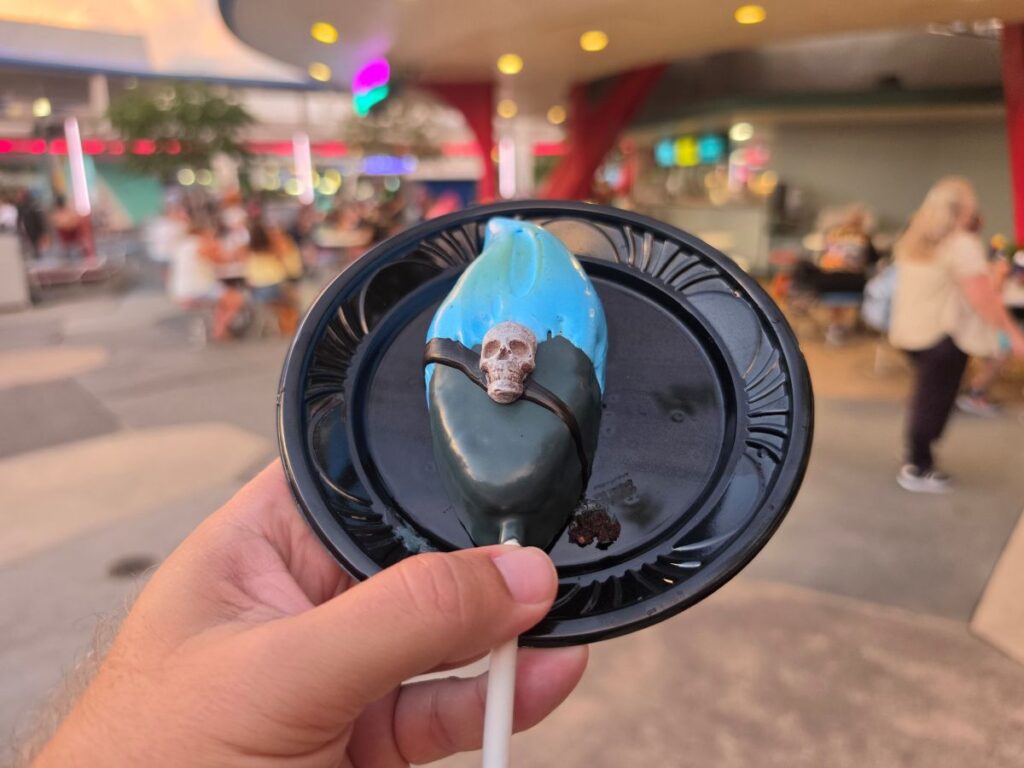 Hand holding a blue and black skull cake pop at Tomorrowland in Magic Kingdom.