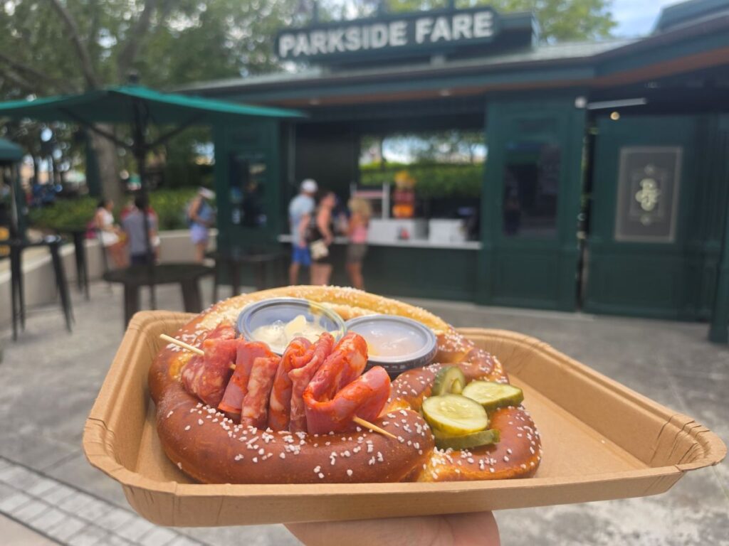 oaded Bavarian Pretzel topped with sliced meats, pickles, and dipping sauces on a cardboard tray in front of Parkside Fare at Universal Studios Florida.