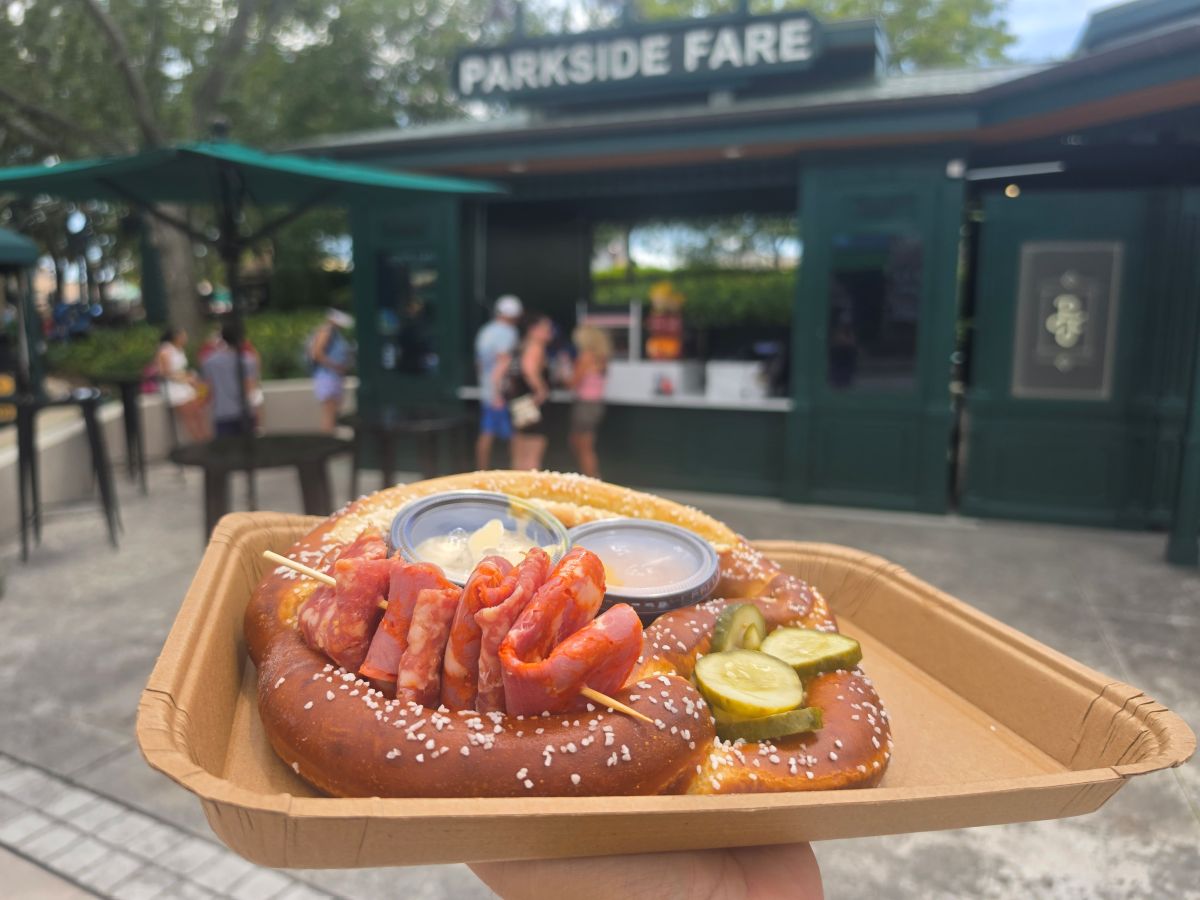 Loaded Bavarian Pretzel topped with sliced meats, pickles, and dipping sauces on a cardboard tray in front of Parkside Fare at Universal Studios Florida.