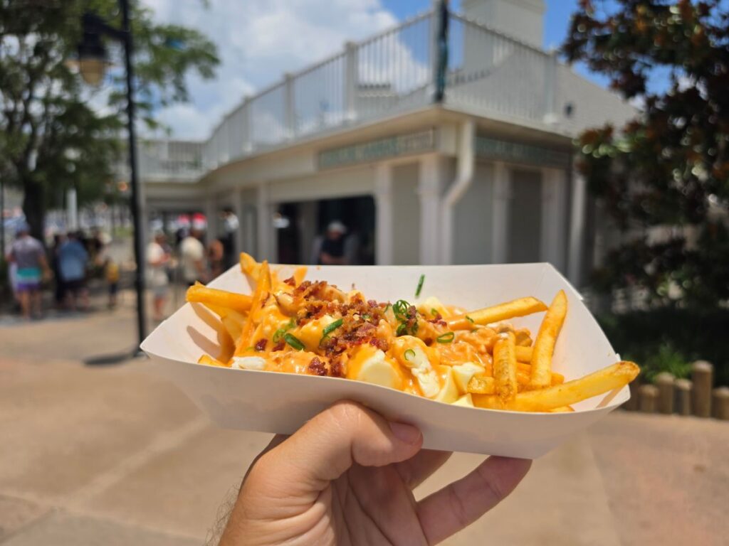 Hand holding Loaded Crab Fries with cheese sauce and bacon bits outside Hurricane Hanna's