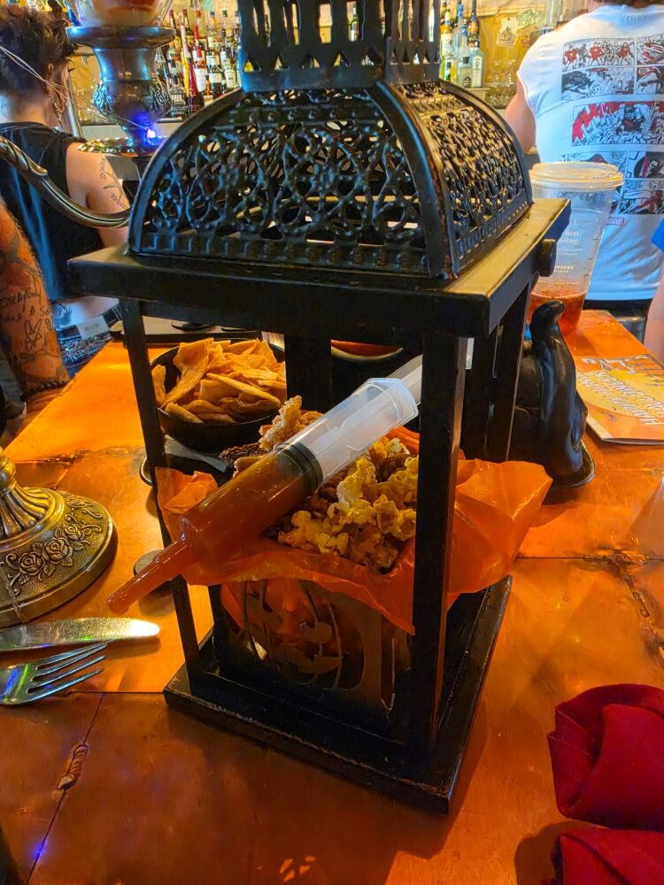 Midnight Mayhem Popcorn Chicken served in a lantern basket with a syringe of hot honey sauce at Jock Lindsey's Hangar Bar.
