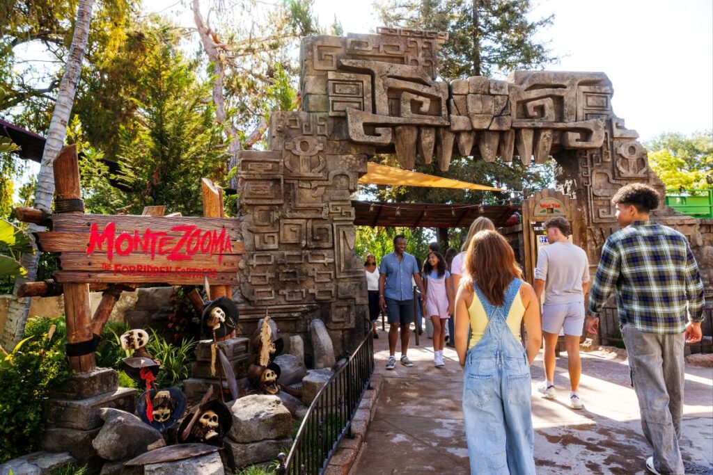 Visitors walk through a stone archway carved with ancient designs at the Montezooma: The Forbidden Fortress attraction entrance at a theme park.
