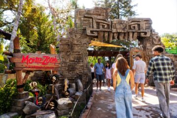 Visitors walk through a stone archway carved with ancient designs at the Montezooma: The Forbidden Fortress attraction entrance at a theme park.