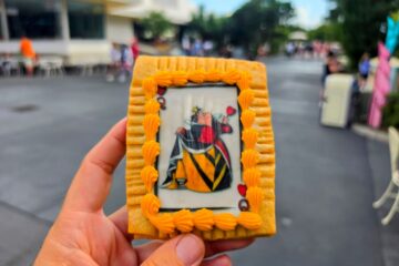 Hand holding a Queen of Hearts Tart in Magic Kingdom with pathways and park walkways in the background.